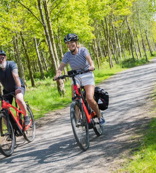 Two people cycle on ebikes through a woodland.